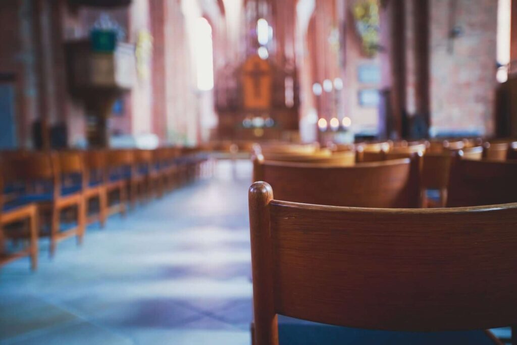 Ein Blick auf Holzst&uuml;hle in einer Kirche, mit einem verschwommenen Altar im Hintergrund.