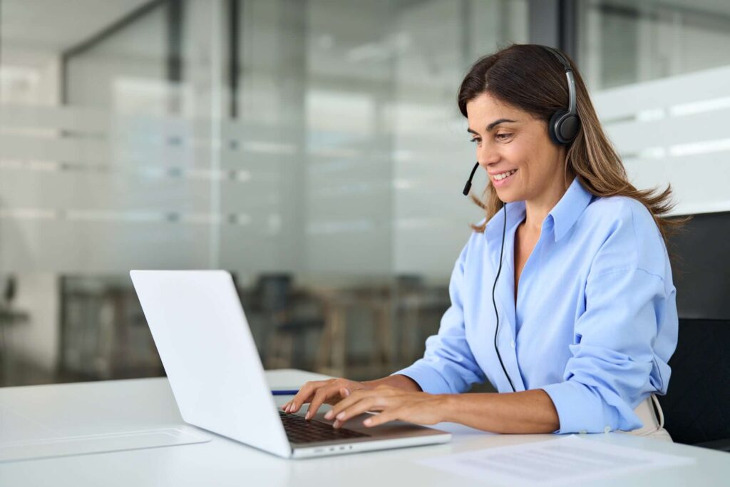 Frau mit Headset, die am Laptop arbeitet, in einem modernen B&uuml;roumfeld.