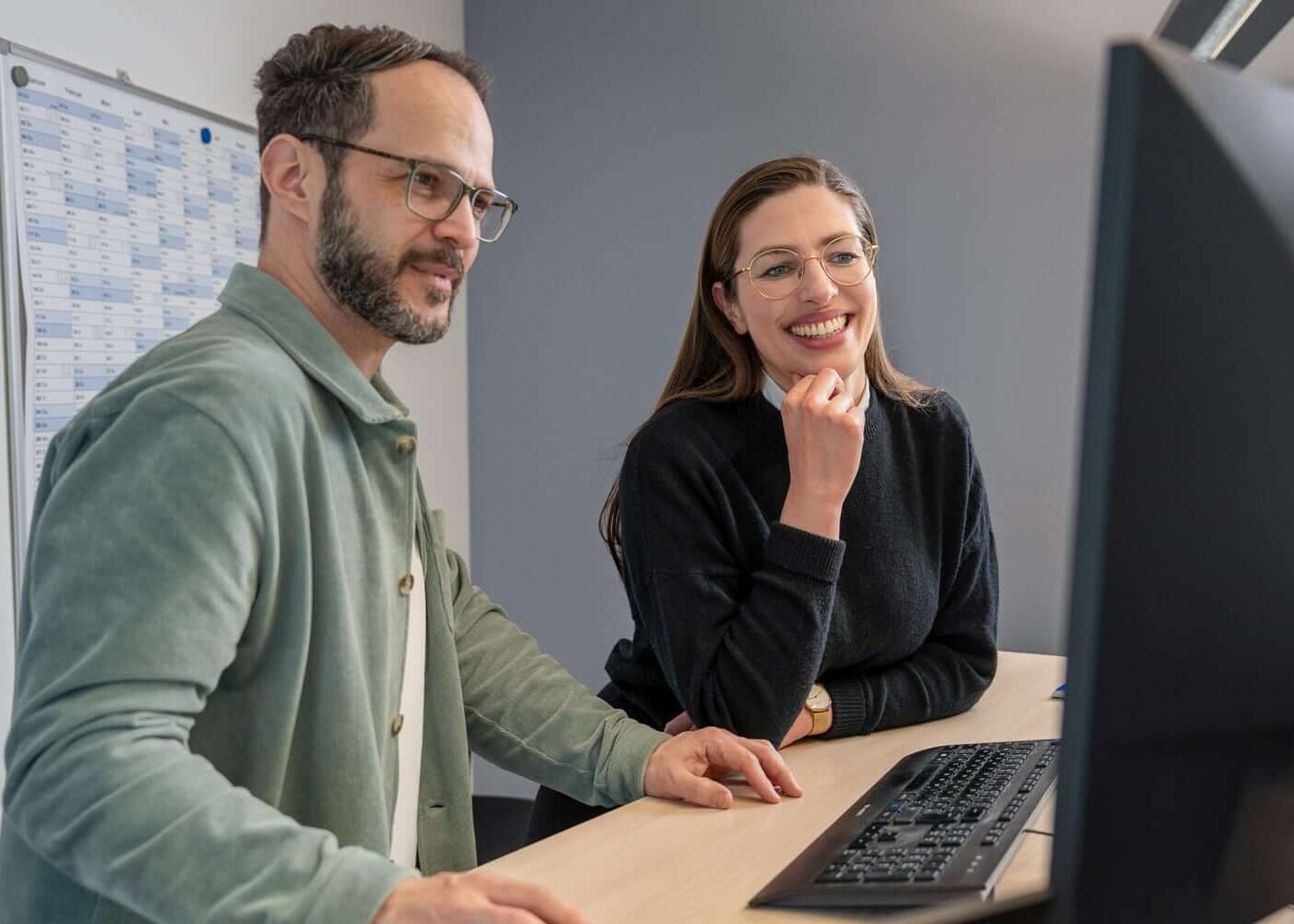 Zwei Datenschutz Consultants beraten sich in Teamarbeit vor einem Computer.