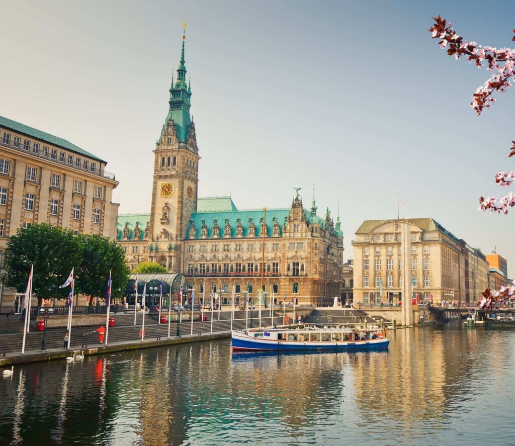 Rathaus Hamburg mit Wasserturm, umgeben von B&auml;umen und Booten im Binnenalster, im fr&uuml;hen Morgenlicht.