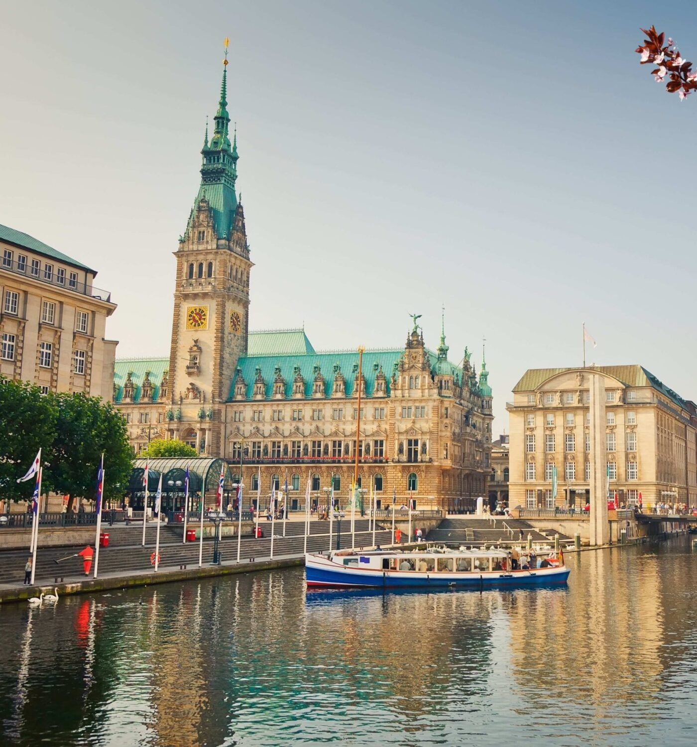 Rathaus Hamburg mit Wasserturm, umgeben von B&auml;umen und Booten im Binnenalster, im fr&uuml;hen Morgenlicht.