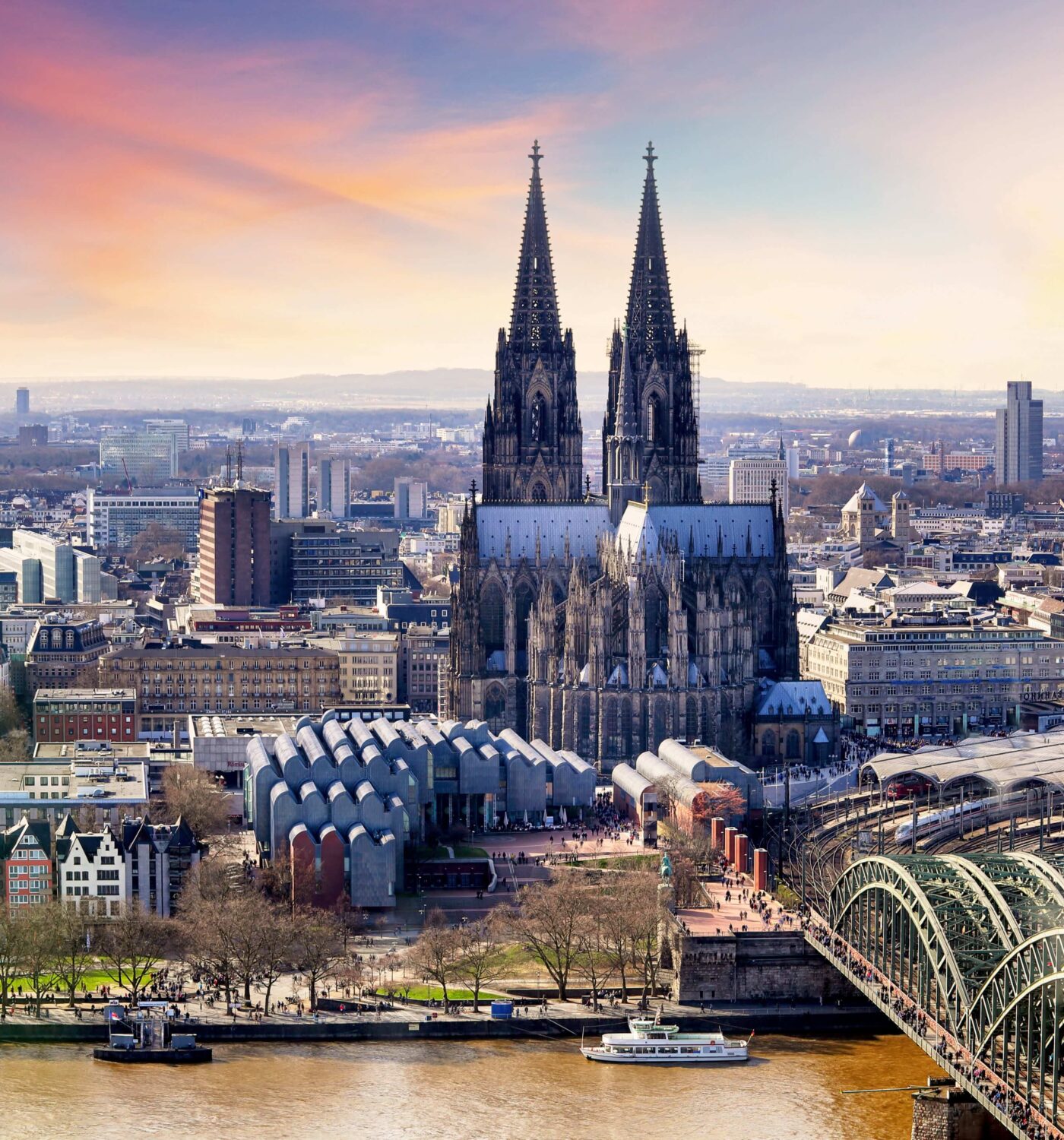 K&ouml;lner Dom mit seinen markanten T&uuml;rmen, umgeben von der Stadtlandschaft und dem Rhein, im Hintergrund der Fernsehturm.