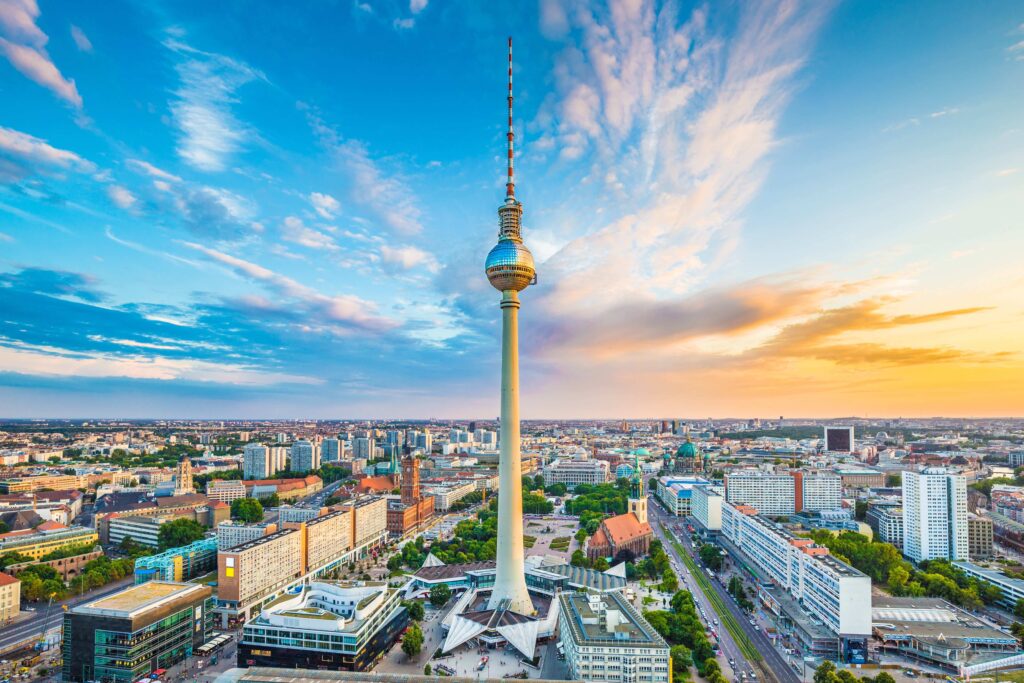 Fernsehturm Berlin bei Sonnenuntergang, umgeben von Stadtlandschaft und Wolken am Himmel.