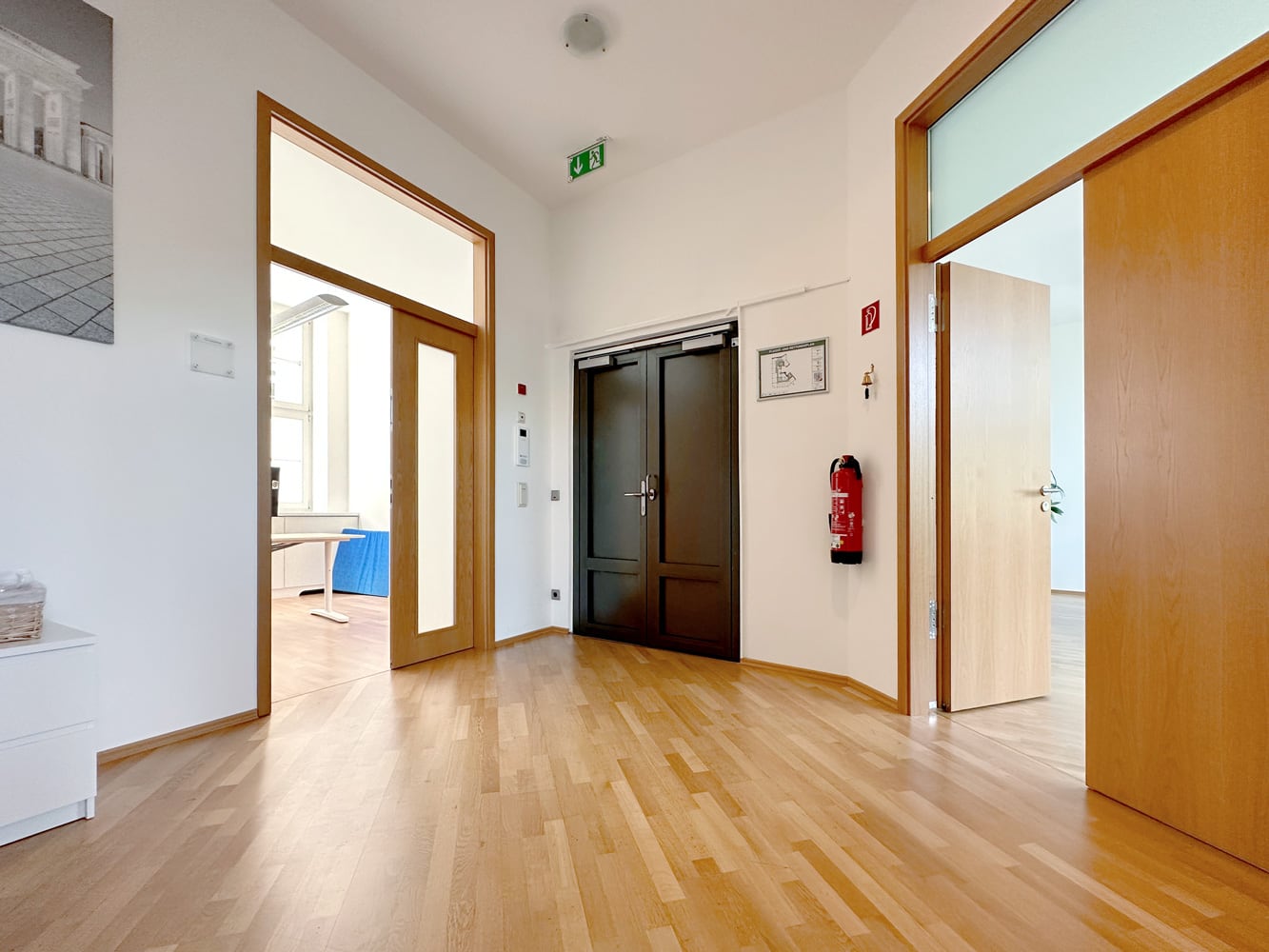 Heller Flur mit Holzfu&szlig;boden, mehreren T&uuml;ren und einem Feuerl&ouml;scher an der Wand.