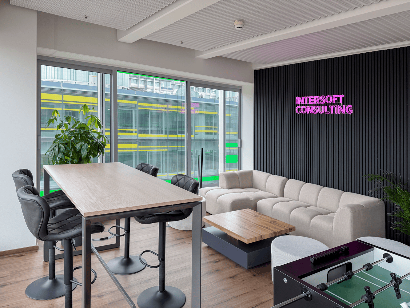 Moderne B&uuml;roumgebung mit einer hellen Sitzecke, einem Tisch und Pflanzen, beschriftet mit "INTERSOFT CONSULTING".