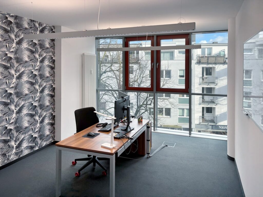 B&uuml;ro mit Holzschreibtisch, Computer, Stuhl und Fenster mit Blick auf eine Stadtansicht. Moderne Einrichtung und Gestaltung.