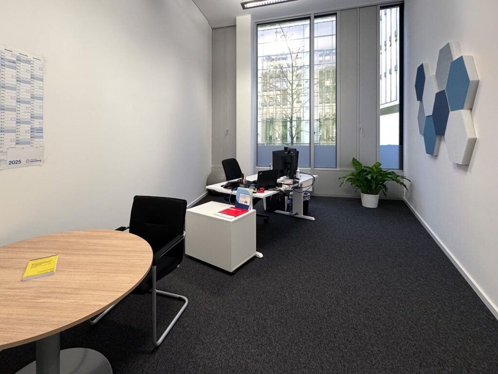 B&uuml;ro mit Schreibtisch, Stuhl und Pflanze, gro&szlig;en Fenstern und hexagonalen Wandpaneelen.