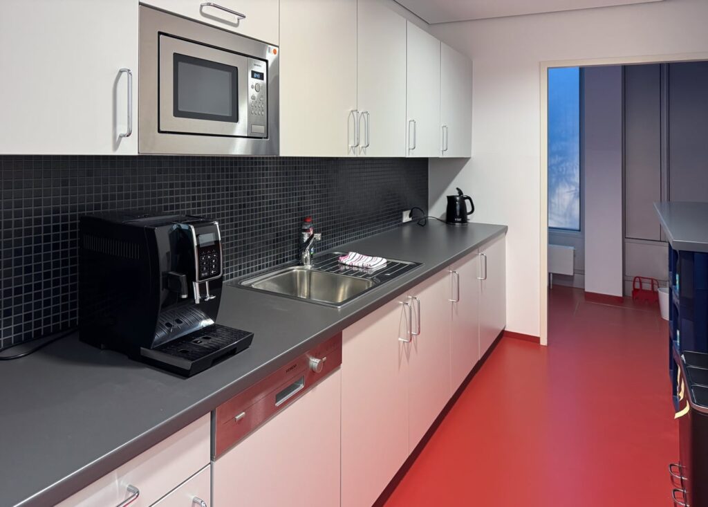 Moderne K&uuml;che mit Mikrowelle, Kaffeemaschine, Sp&uuml;le und rotem Bodenbelag.