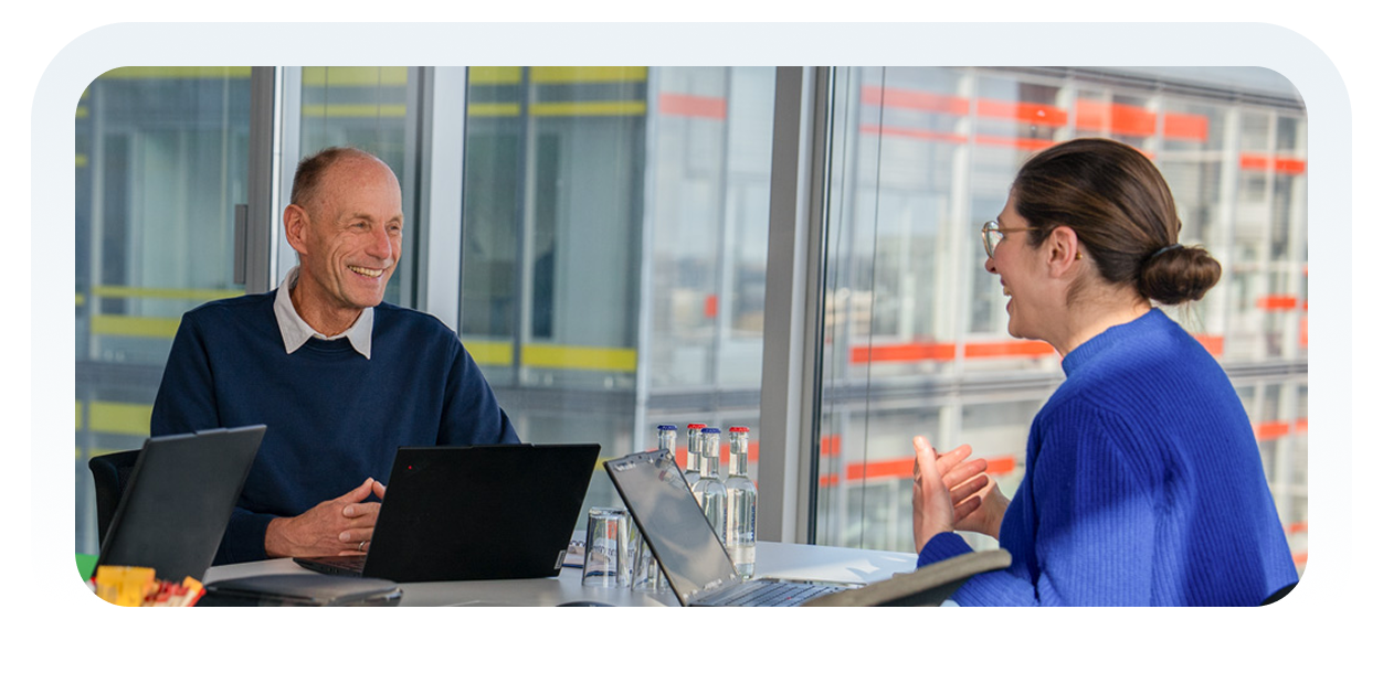 Zwei Personen in einem modernen Büro im Gespräch, mit Laptops und Wasserflaschen auf dem Tisch.